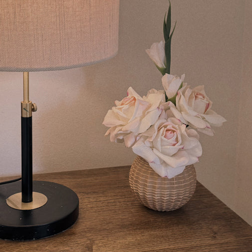 Blush pink rose arrangement in a textured vase beside a table lamp