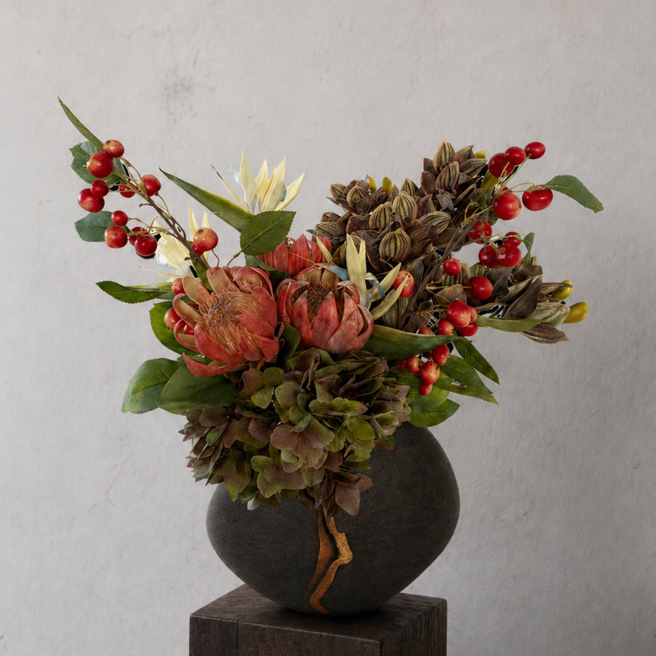 Curated artificial stems in red, green and cream tones styled in a dark vase